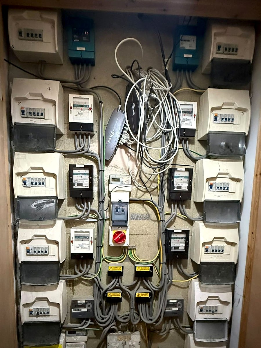 A communal meter cupboard with a bank of meters and consumer units, opened for maintenance